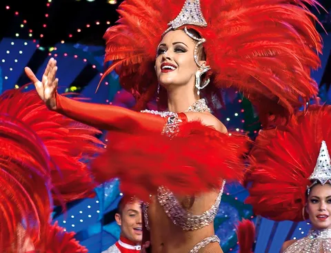 Biglietti Moulin Rouge: ballerina con copricapo di piume rosse e paillettes sotto le luci del palco