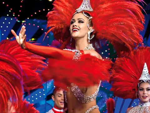 Bilhetes Moulin Rouge: dançarina com cocar de penas vermelhas e paetês sob as luzes do palco