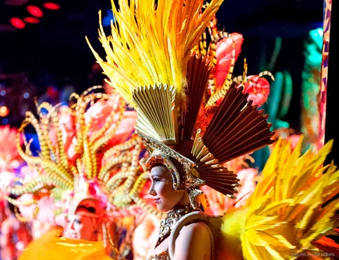 Entradas Moulin Rouge: bailarina con tocado de plumas doradas y corona de abanico en el escenario