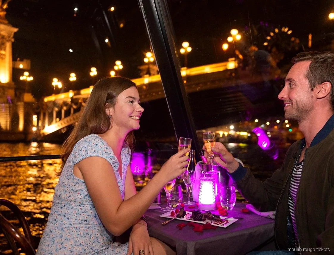 Paar stößt beim abendlichen Dinner auf der Seine mit Champagner an, vor der Show mit Moulin Rouge Tickets
