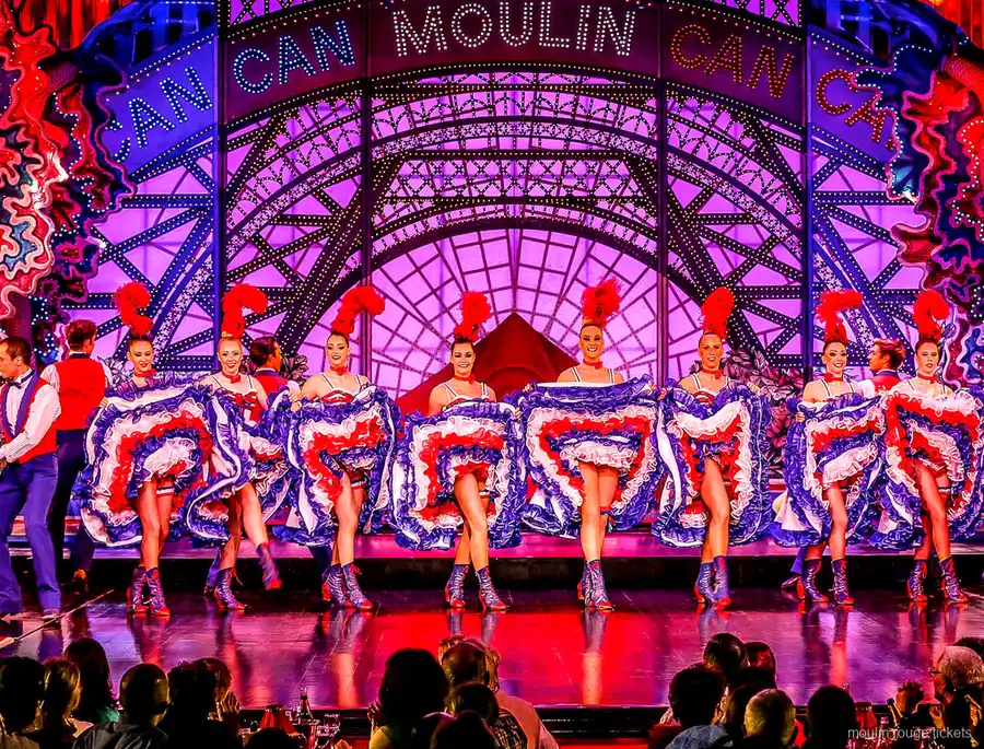 Fila de French Cancan con faldas tricolores bajo el letrero luminoso Moulin, entradas Moulin Rouge