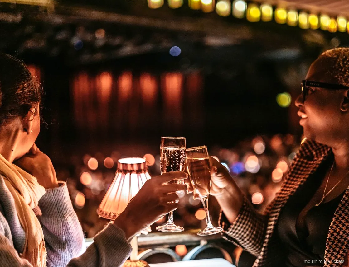 Two guests toasting with champagne at a lamp-lit table, Moulin Rouge tickets for the evening show