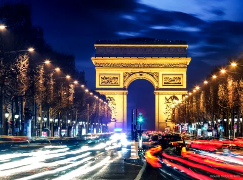 Arc de Triomf il·luminat de nit al final dels Camps Elisis amb rastres de llum, ruta abans de les entrades al Moulin Rouge