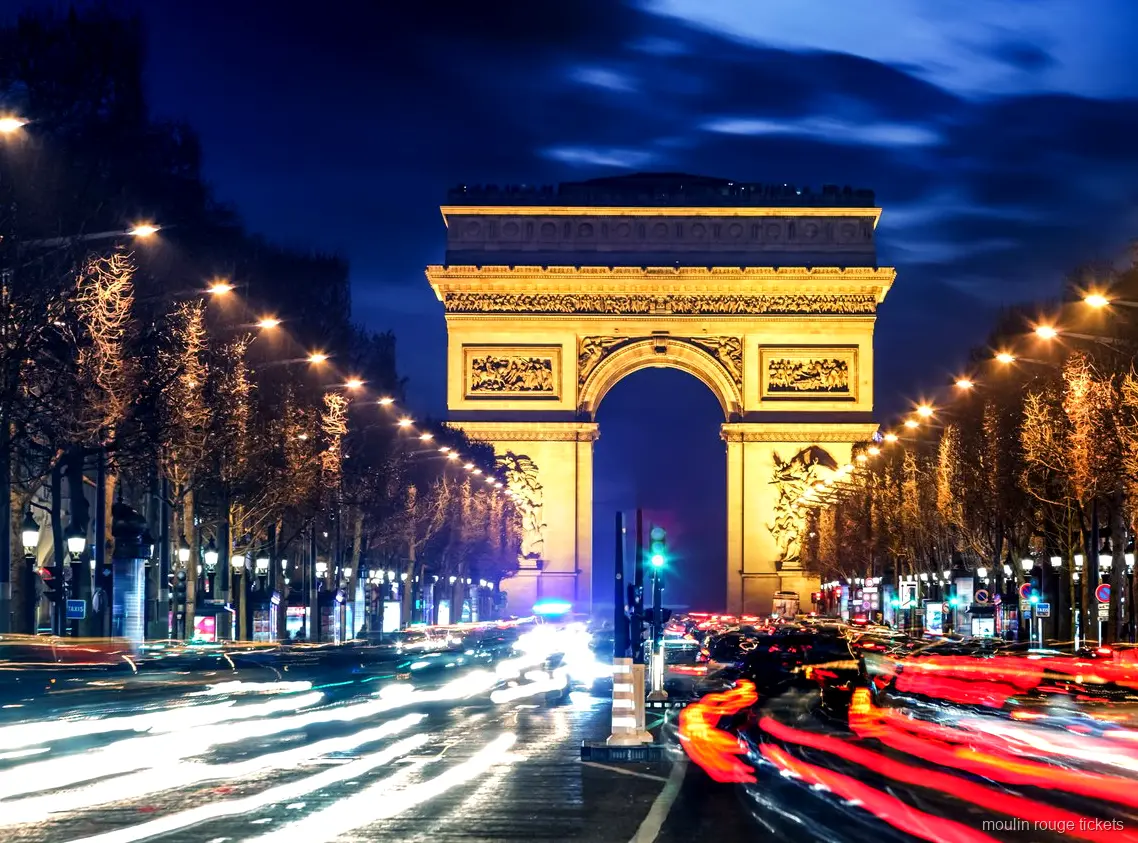 Arco del Triunfo iluminado de noche al final de los Campos Elíseos con estelas de luz, antes de las entradas Moulin Rouge